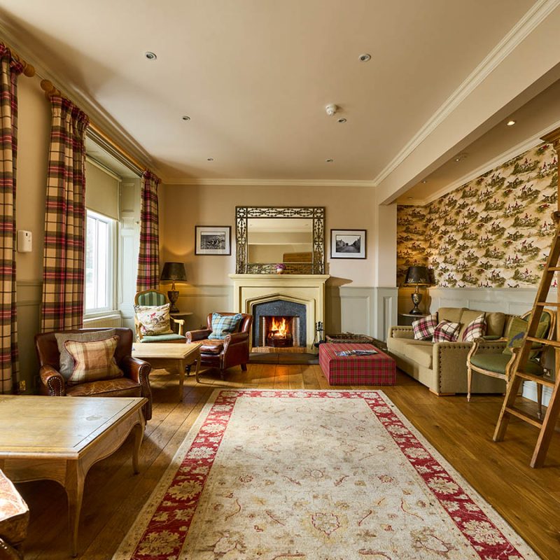 The library with books on shelves, seating and a fireplace at the Ulbster Arms Hotel