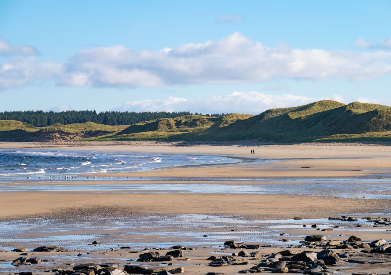 Dunnet Bay beach on the North Coast 500 in Caithness with two people walking along the beach.